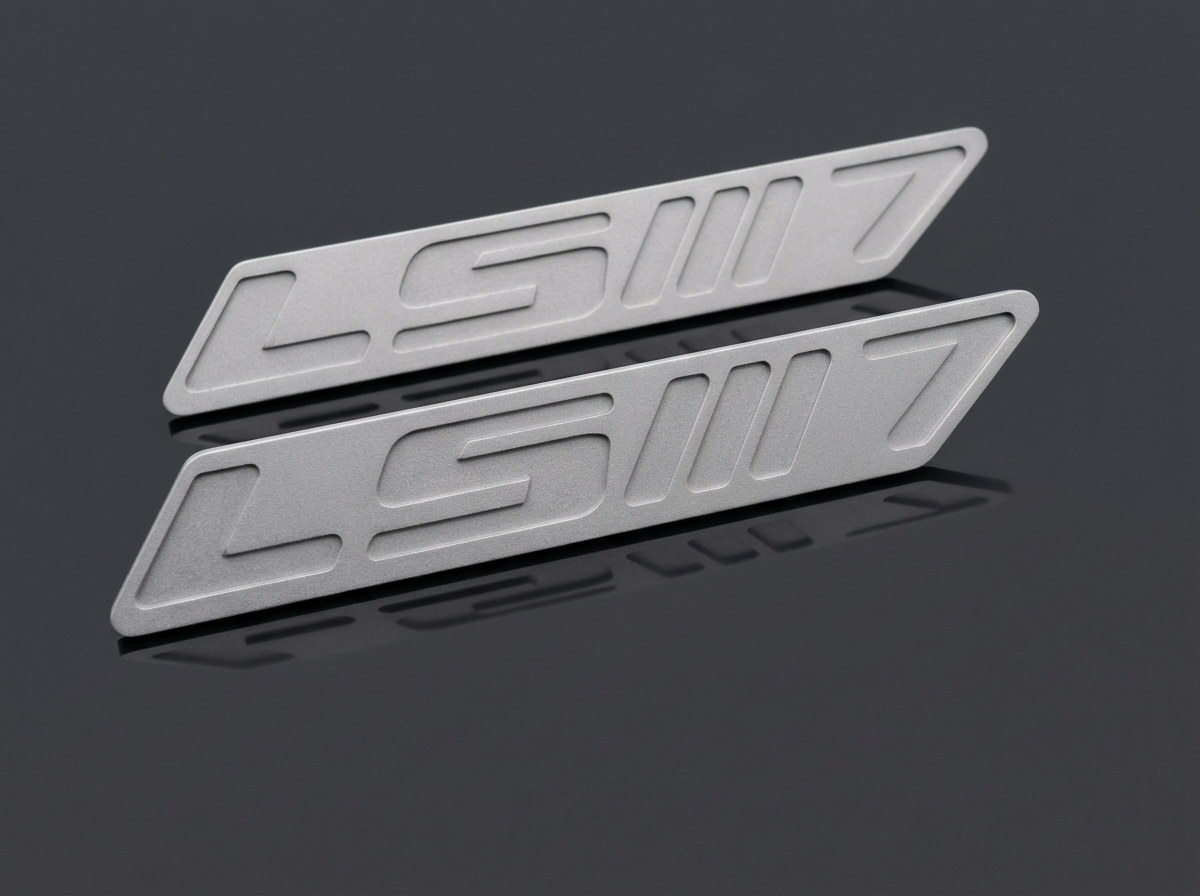 Raw sandblasted aluminum LS X Dct 7 speed emblem pair, studio photo